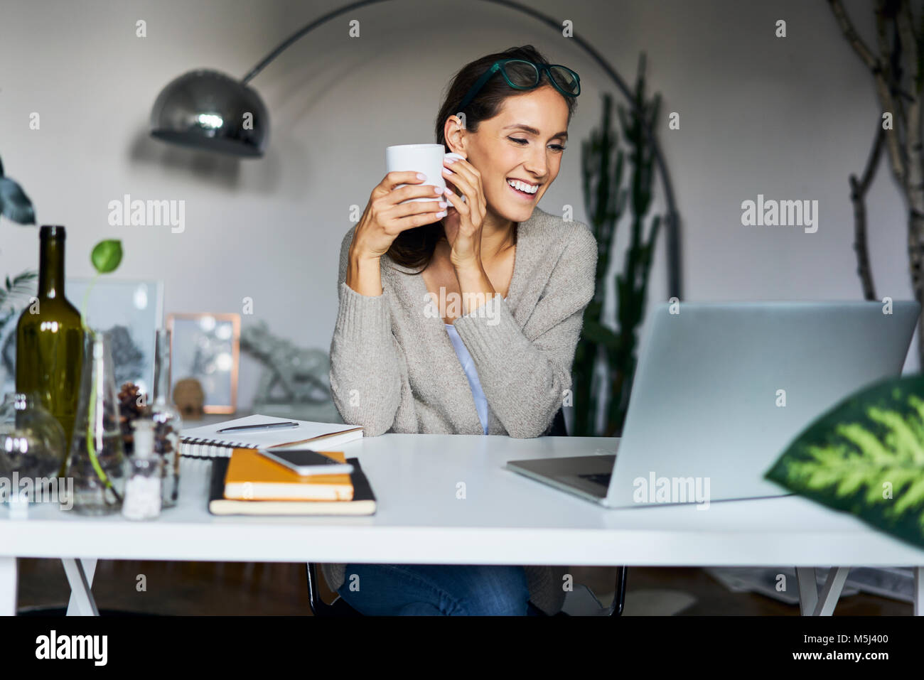 Happy young woman at home with laptop on desk Stock Photo - Alamy