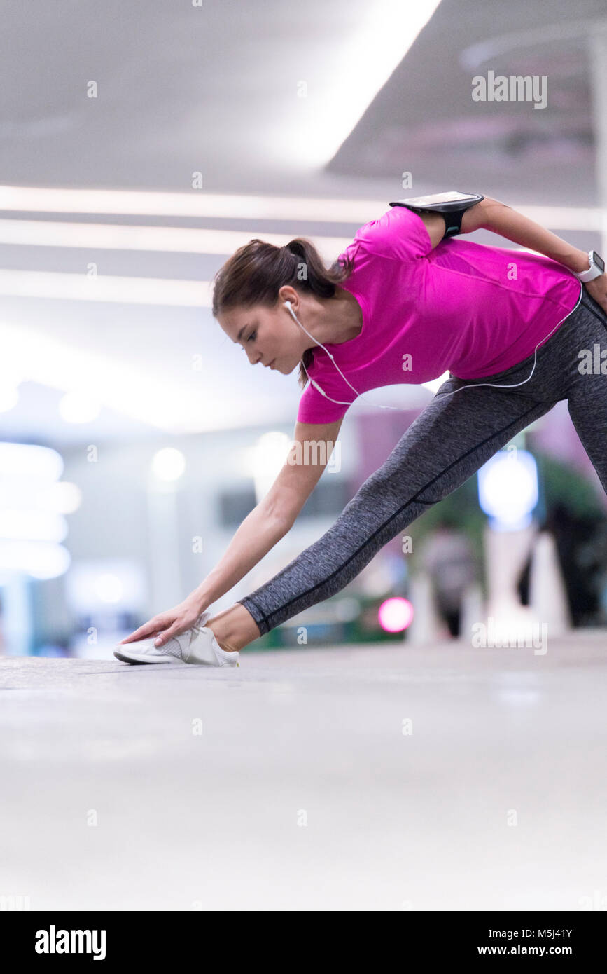 Young woman in pink sportshirt listening to music and stretching in front of modern building Stock Photo
