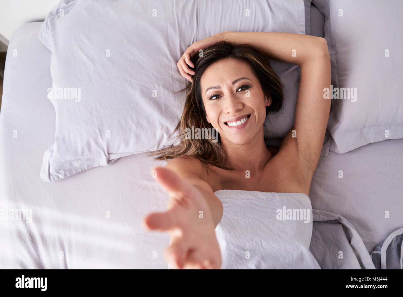 Portrait of happy asian lady giving a hand and lying on the bed. Stock Photo