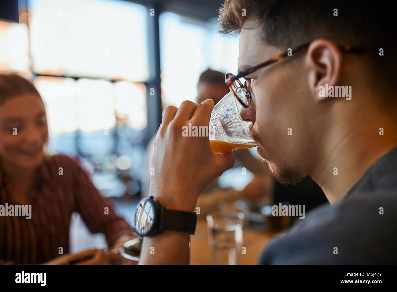 Young man drinking glass of juice in a cafe with friends in background Stock Photo