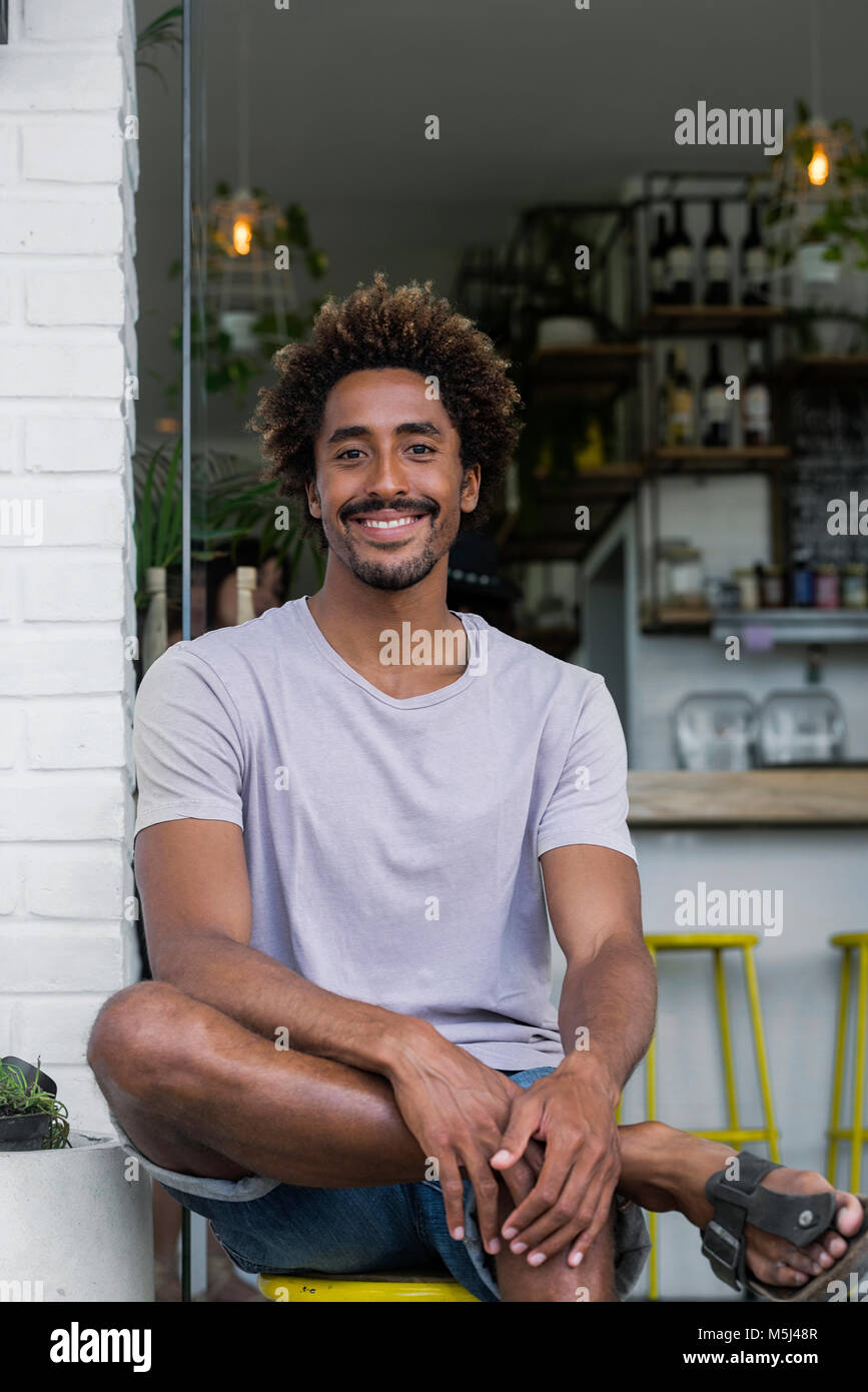 Portrait of smiling man sitting in front of a cafe Stock Photo