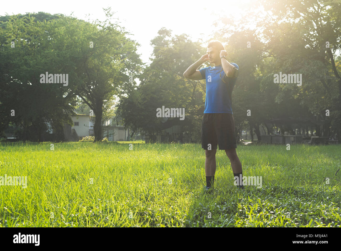 Runner standing in urban park, wearing headphones Stock Photo
