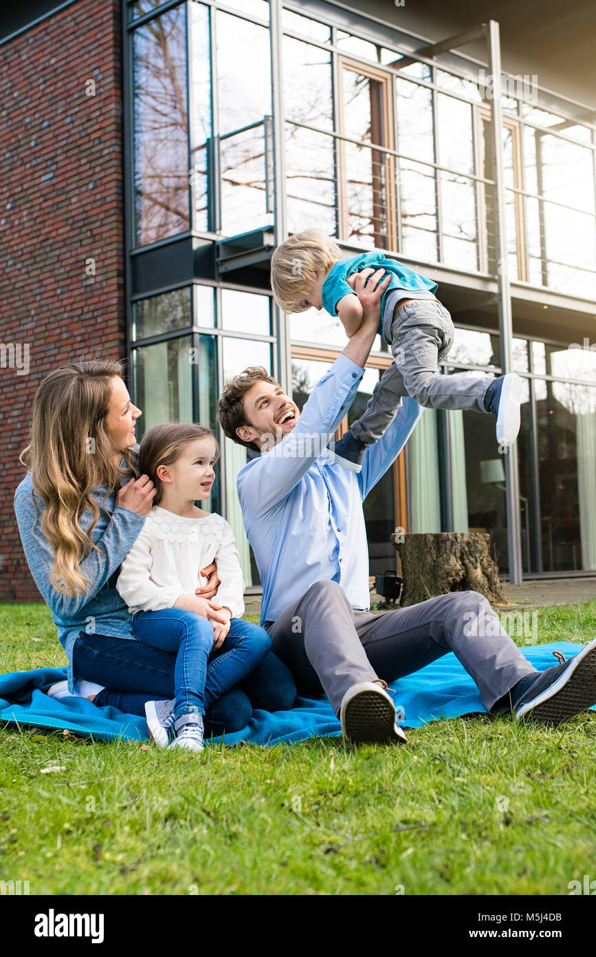 Happy family on blanket in garden in front of their home with father litfting up son Stock Photo