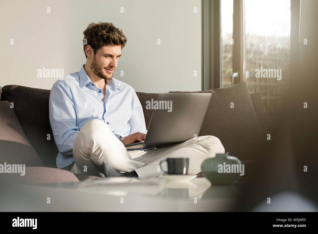 Man sitting on couch at home using laptop Stock Photo