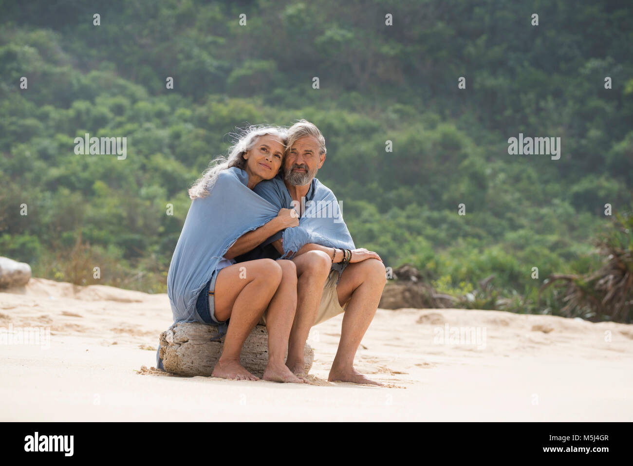 Senior couple sitting on the beach, wrapped in a blanket Stock Photo