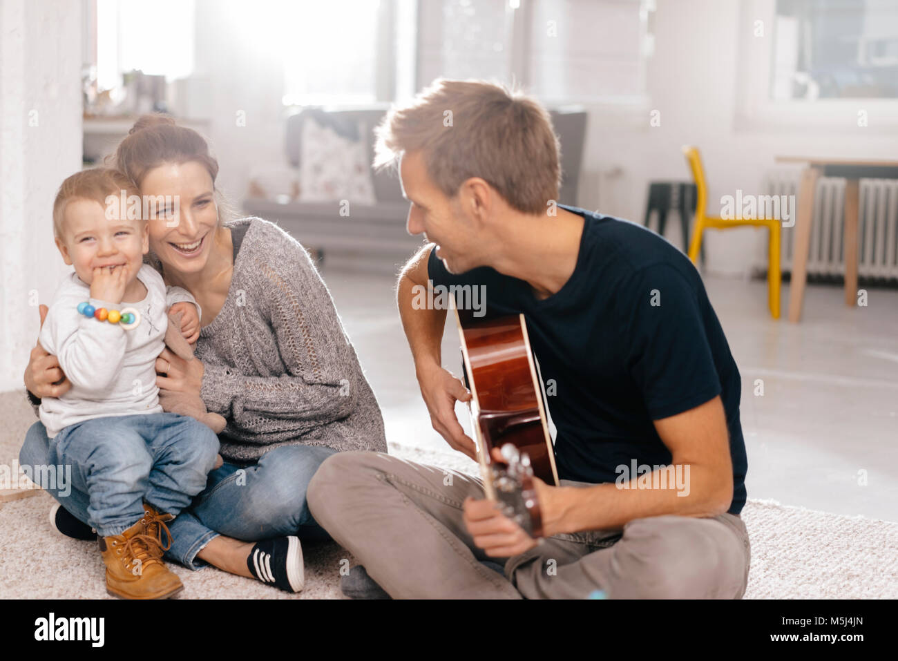 Happy family sitting on the floor with father playing guitar Stock Photo