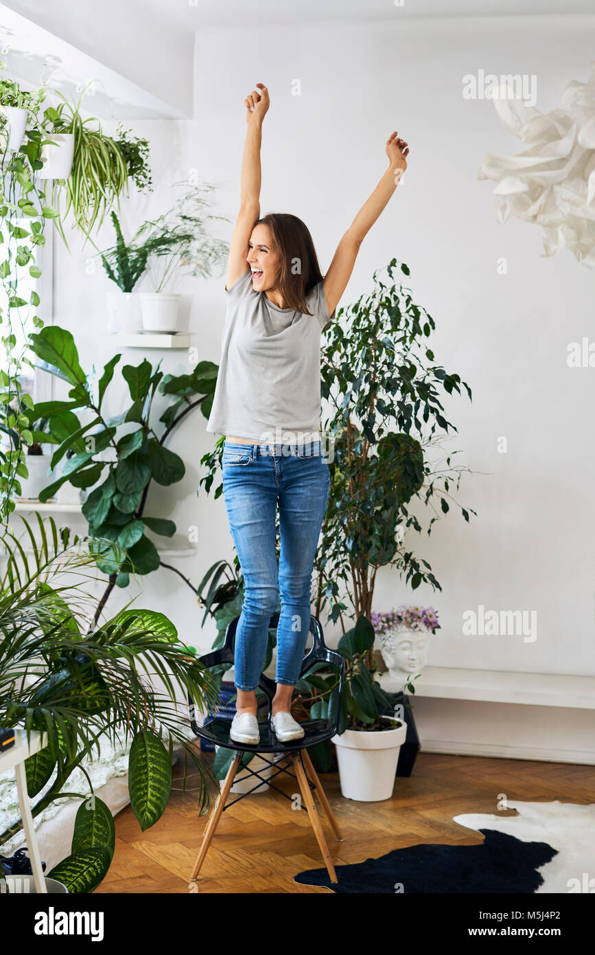 Young woman standing on chair in a room cheering Stock Photo