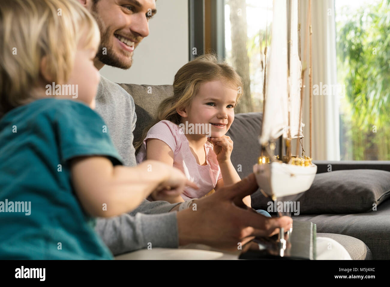 Smiling father and children looking at toy model ship on couch at home Stock Photo