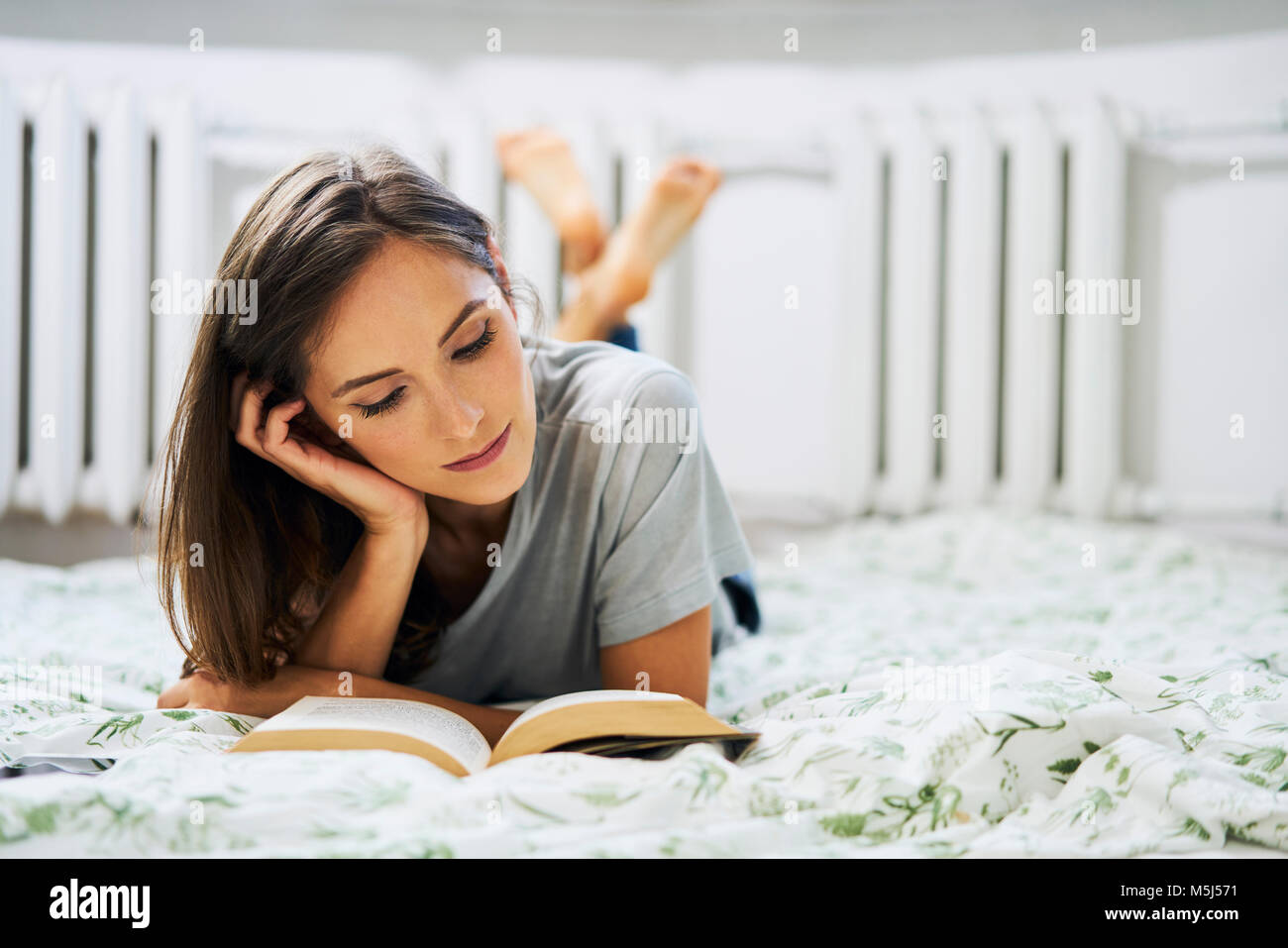 Young woman at home lying in bed reading book Stock Photo