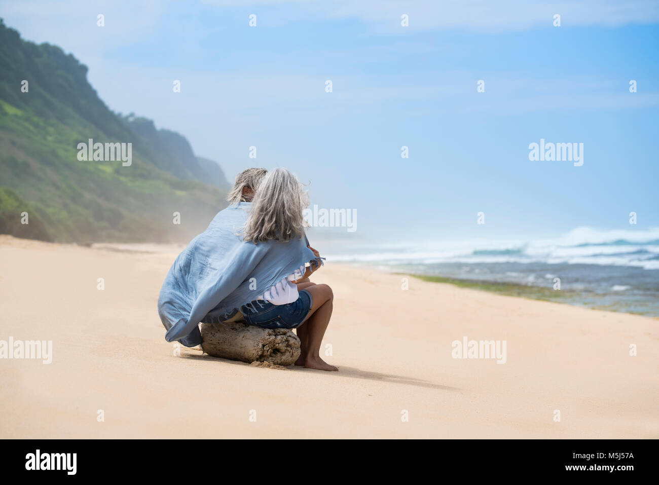 Senior couple sitting on the beach, wrapped in a blanket Stock Photo