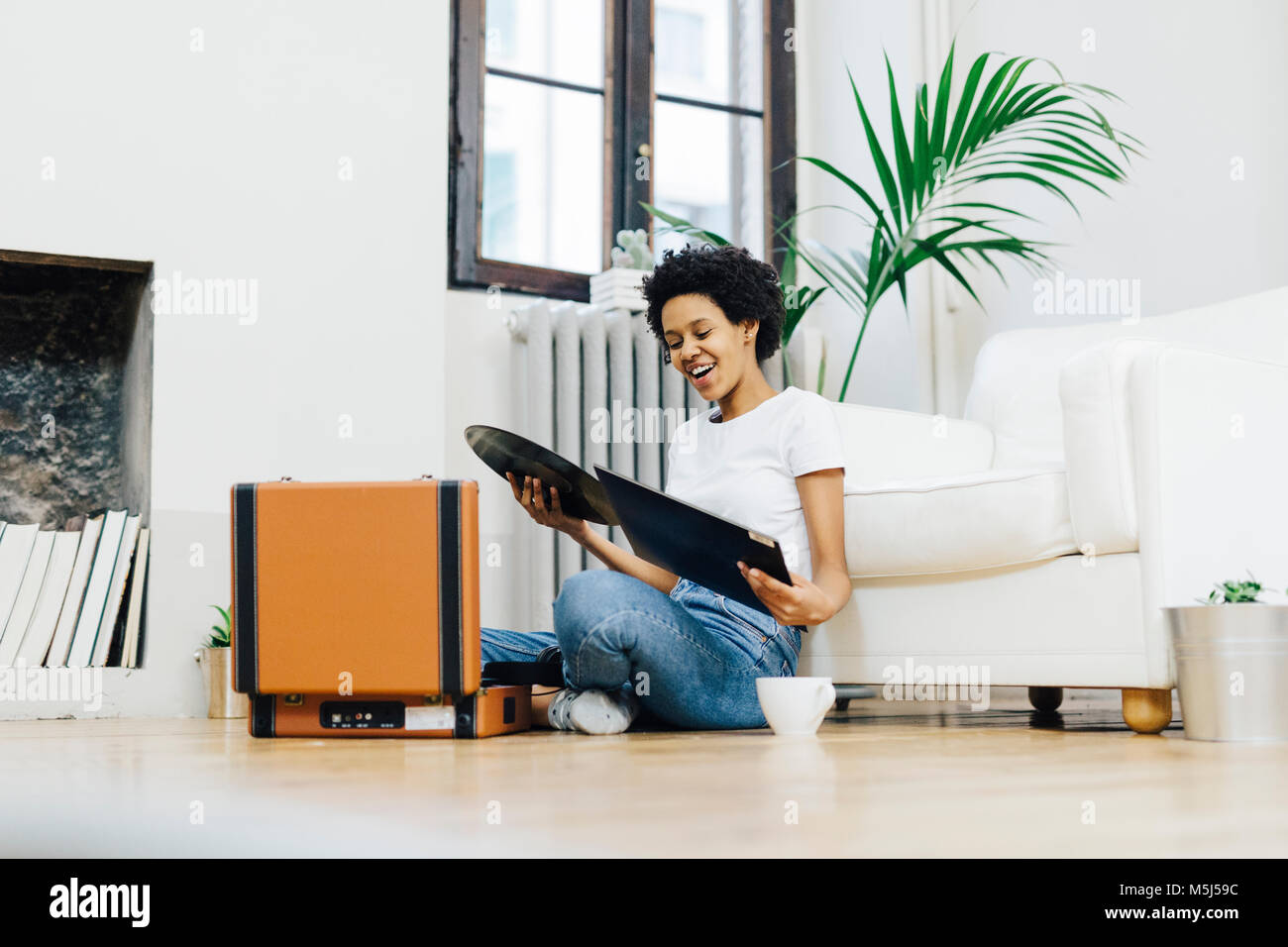 Young woman sitting on grounf listening music from record player Stock Photo
