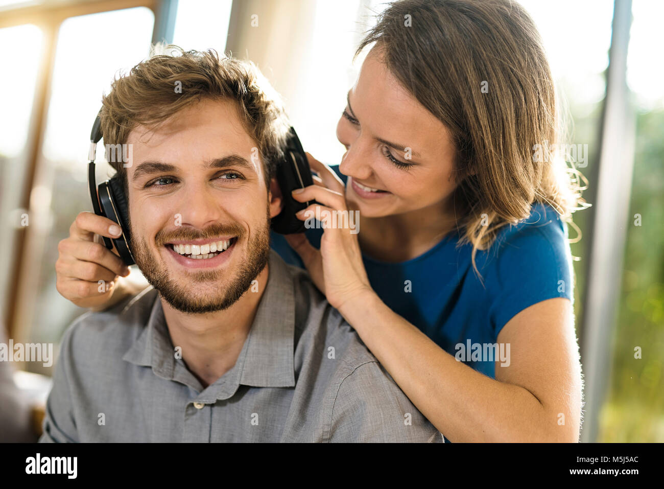Smiling woman putting on headphones on boyfriend Stock Photo