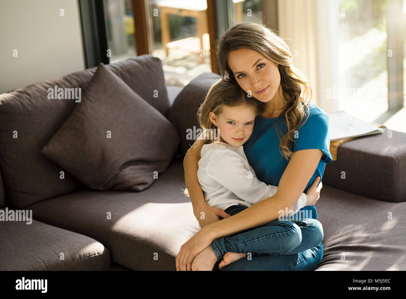 Portrait of smiling mother holding her daughter on sofa at home Stock Photo
