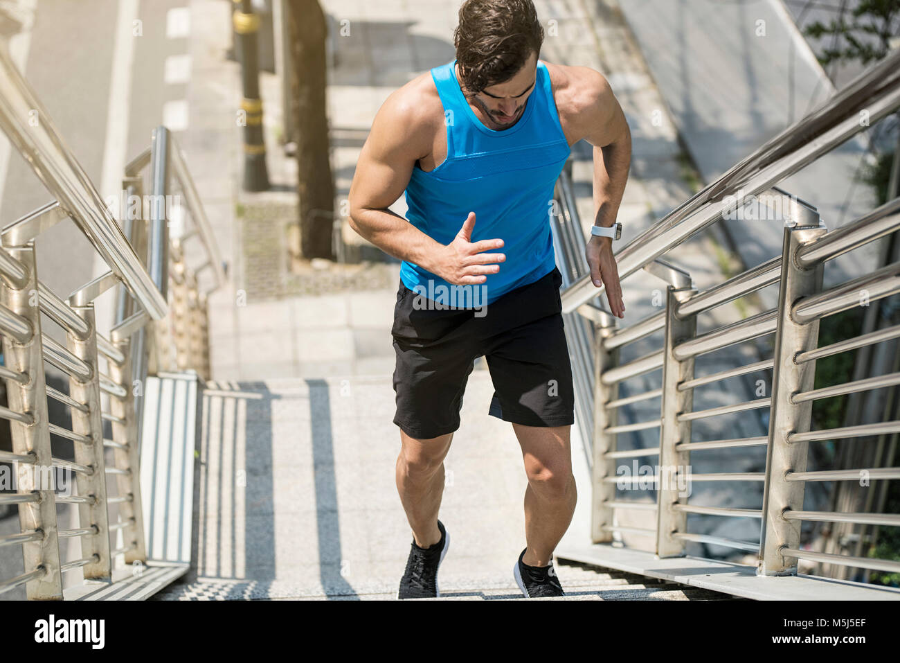 Man in blue fitness shirt running upstairs in city Stock Photo