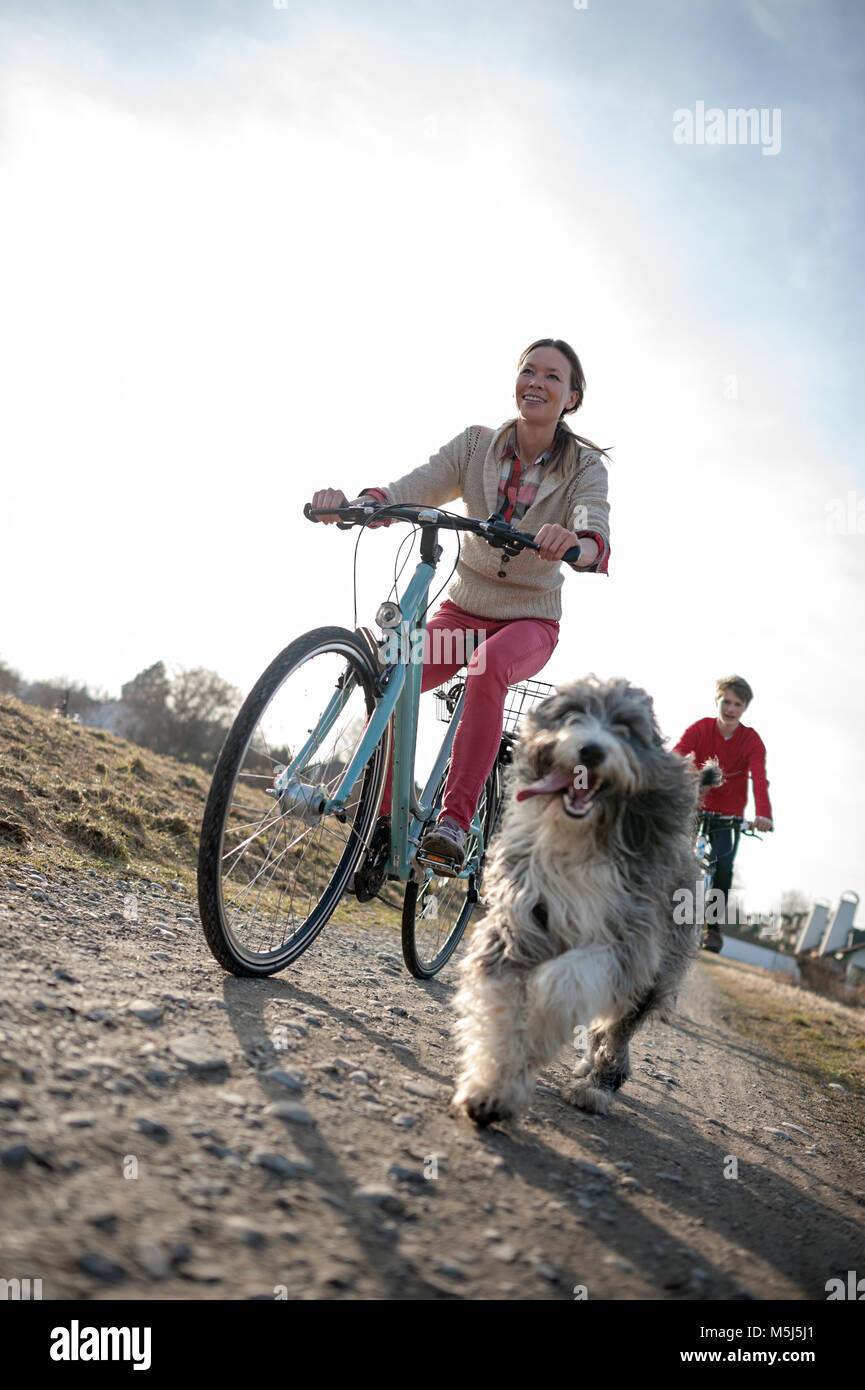 Man and woman with dog riding bicycle on dirt track Stock Photo
