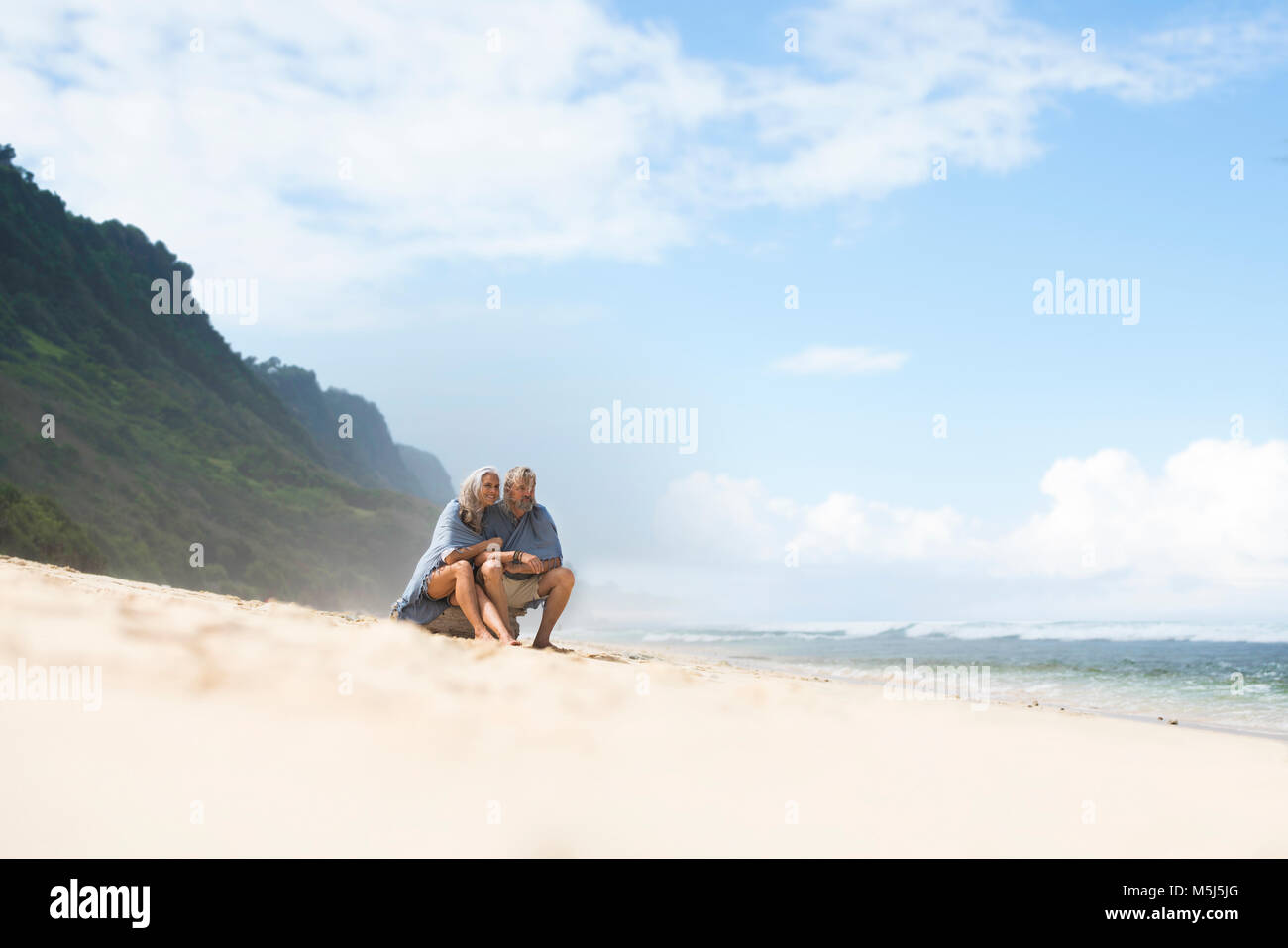 Senior couple sitting on the beach, wrapped in a blanket Stock Photo