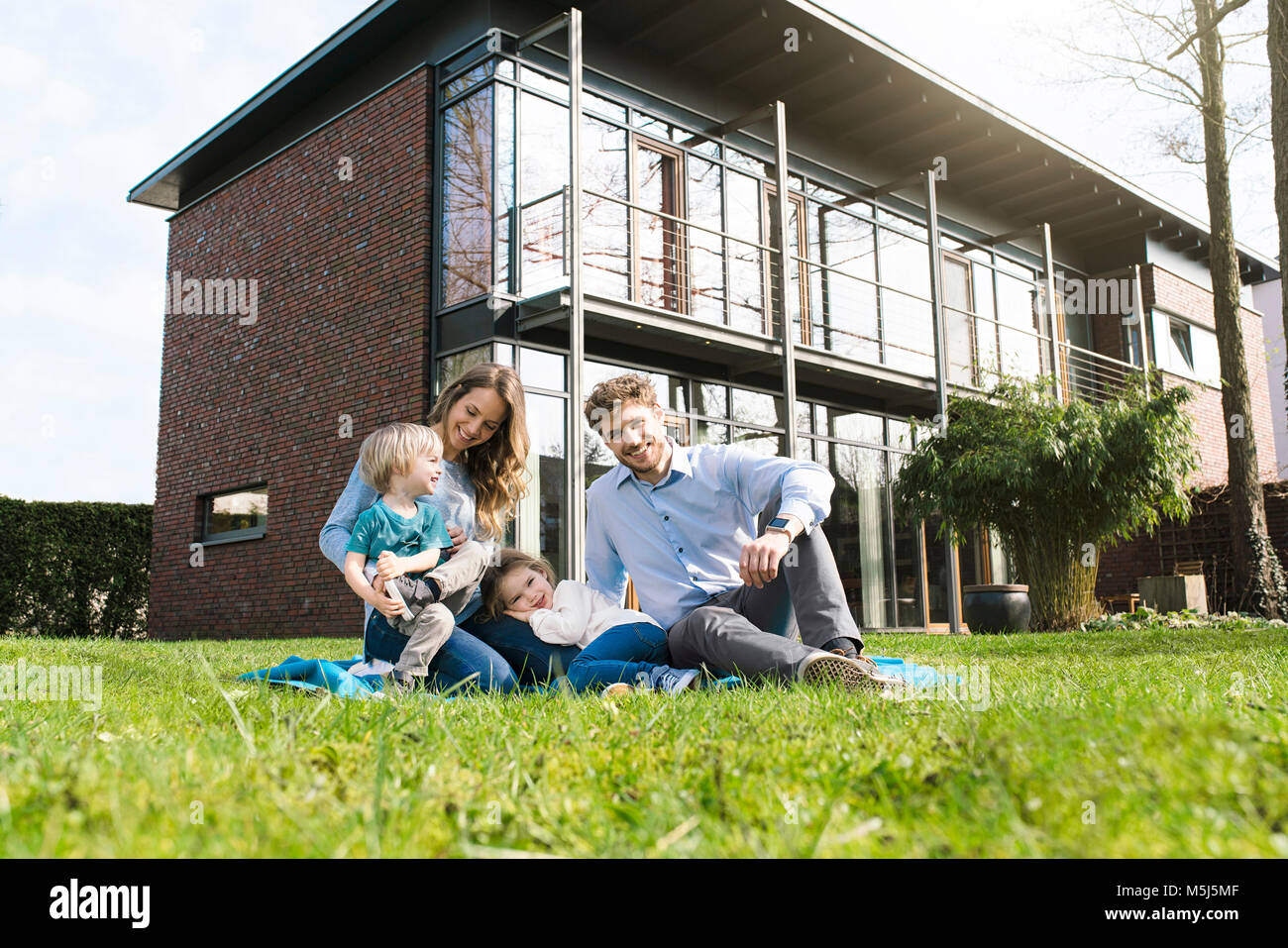 Portrait of smiling family on blanket in garden in front of their home Stock Photo