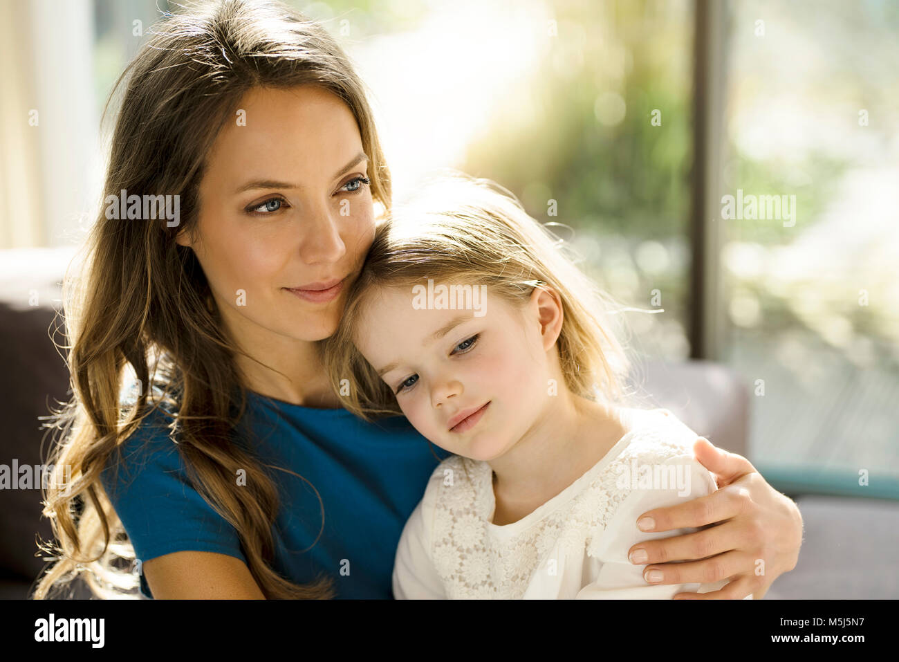 Portrait of smiling mother holding her daughter  in front of window Stock Photo