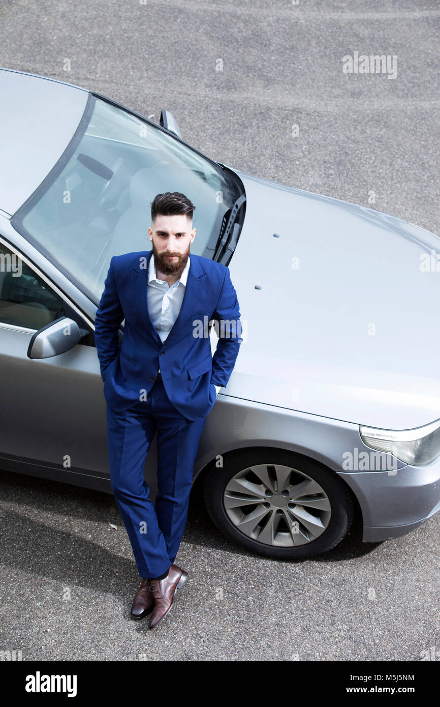 Young man wearing suit, leaning against new car Stock Photo