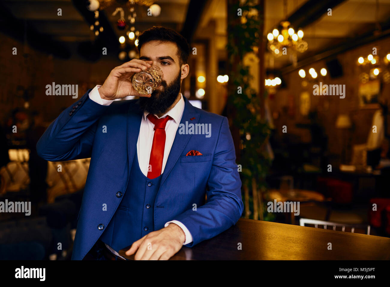 Eegant young man in a bar drinking from tumbler Stock Photo