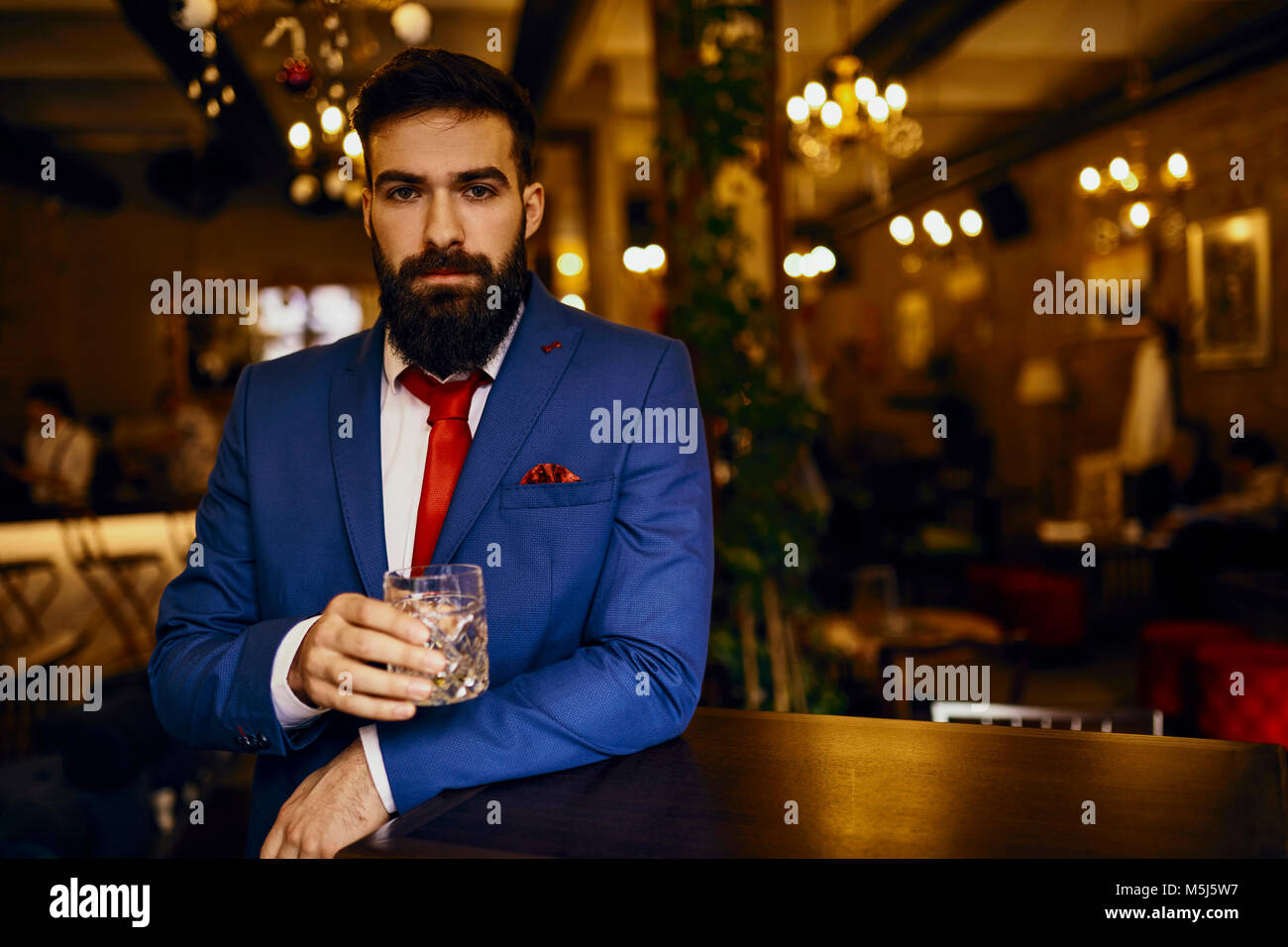 Portrait of elegant young man in a bar holding tumbler Stock Photo