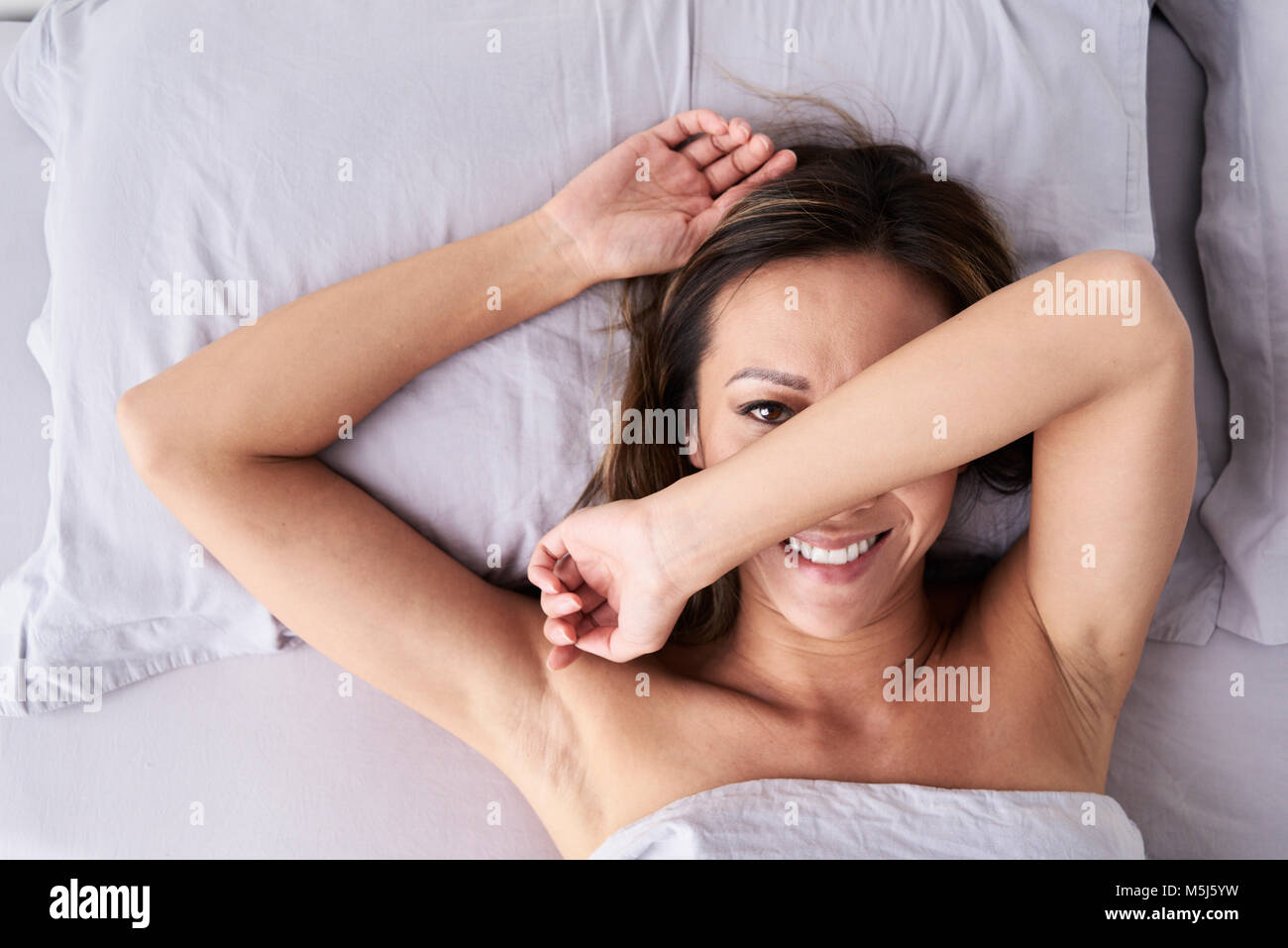Portrait of happy asian lady hidding face and lying on the bed. Stock Photo