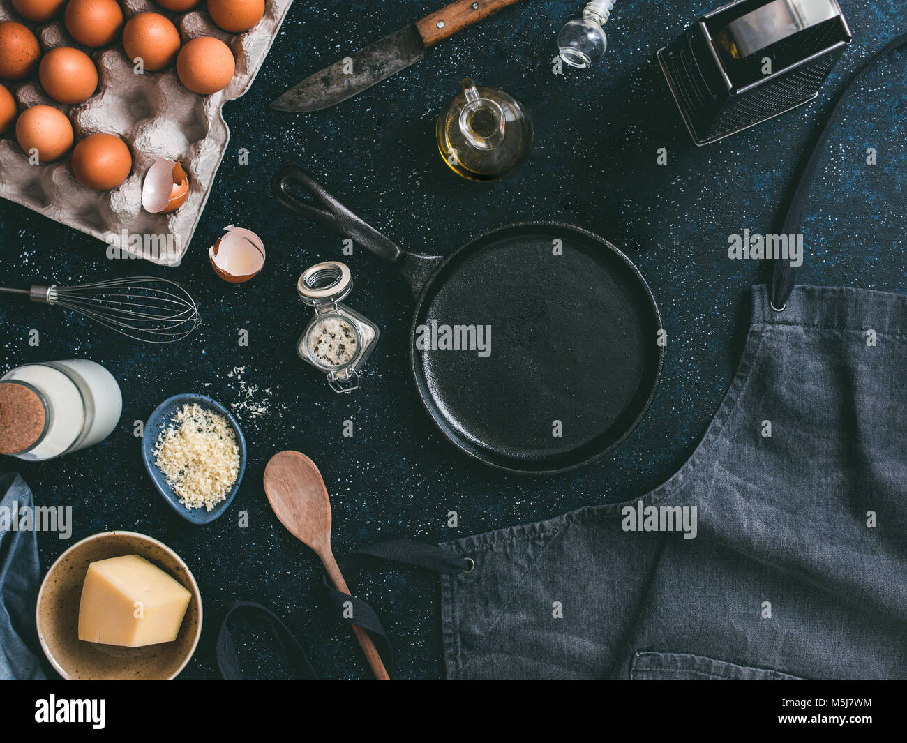 Empty cast-iron frying pan and ingredients for omlette or scrambled eggs,top view.Egg,shell,milk,parmesan cheese,scented rosemary salt,olive oil,peppe Stock Photo