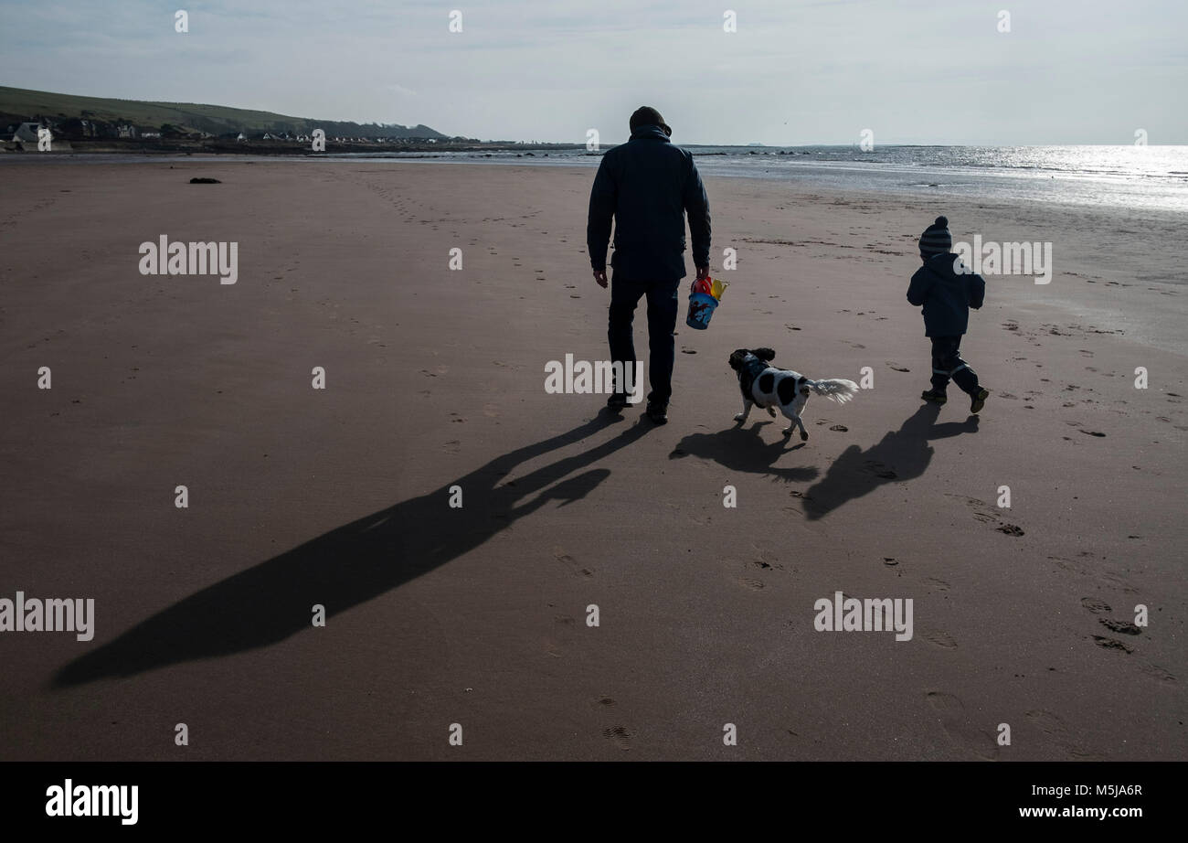 A father and son with their dog running on a deserted beach at Seamill, Ayrshire, Scotland. Stock Photo