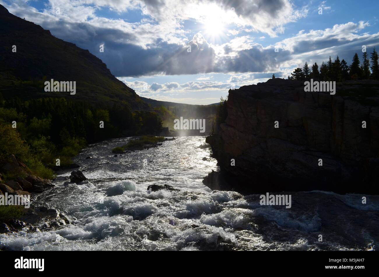 A small mountain river, flows quickly down stream, over sharp, jagged rocks, while the sun rises in the distance, reflecting the steam from below Stock Photo