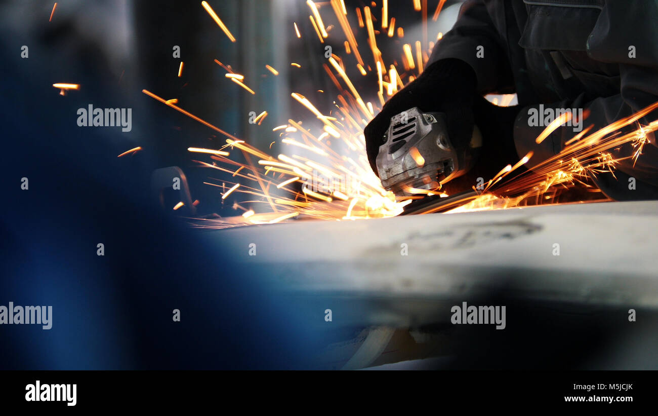 Car service worker grinding metal construction with a circular saw