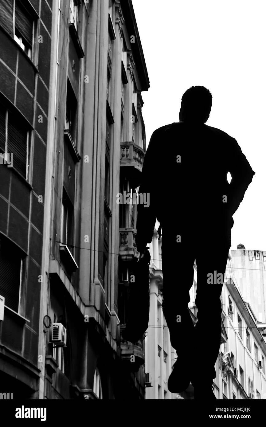 Silhouette of a young man walking and city architecture in black and white low angle view Stock Photo
