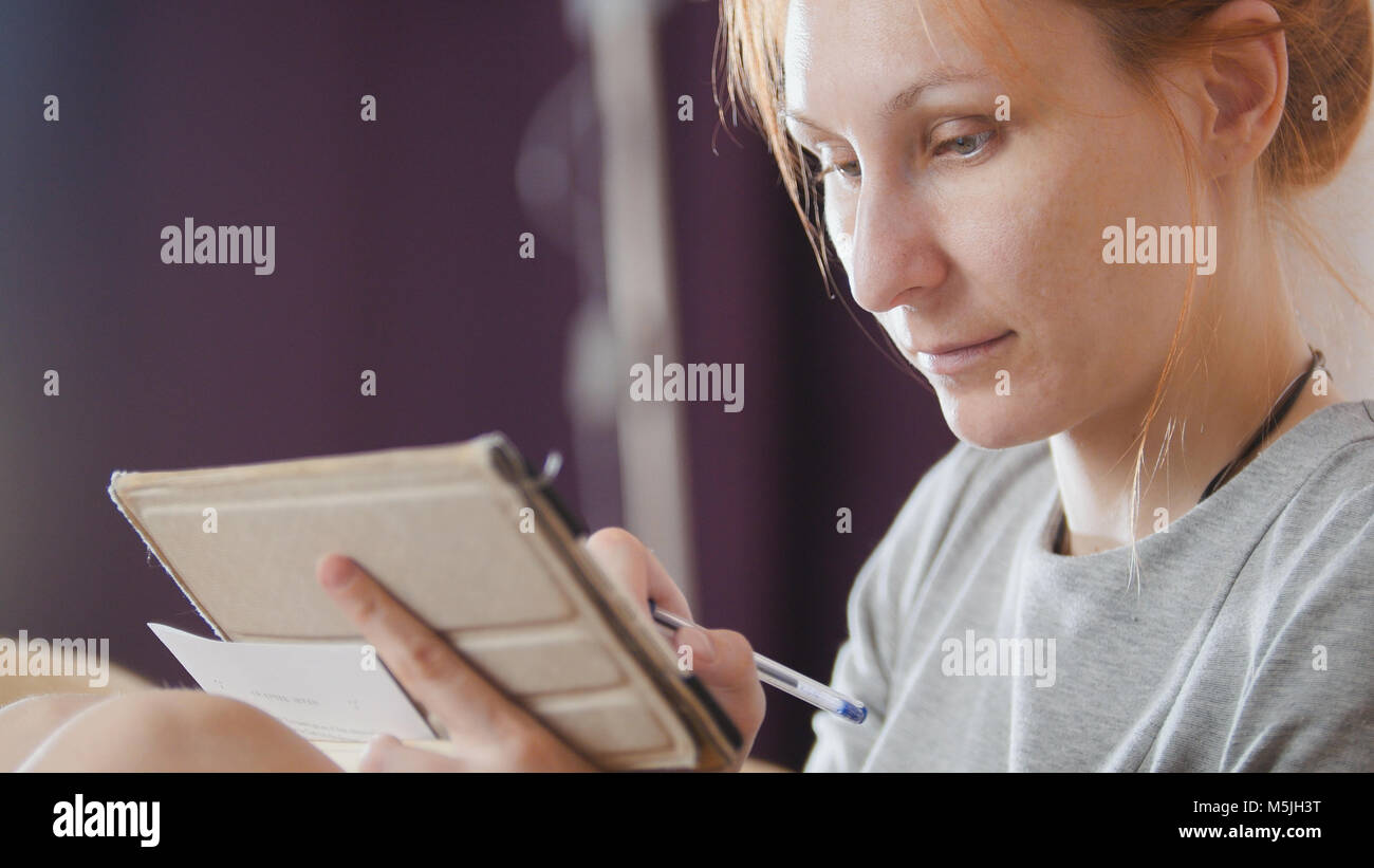 Portrait of a pretty woman at home sitting at sofa and working with gadget and notebook Stock Photo