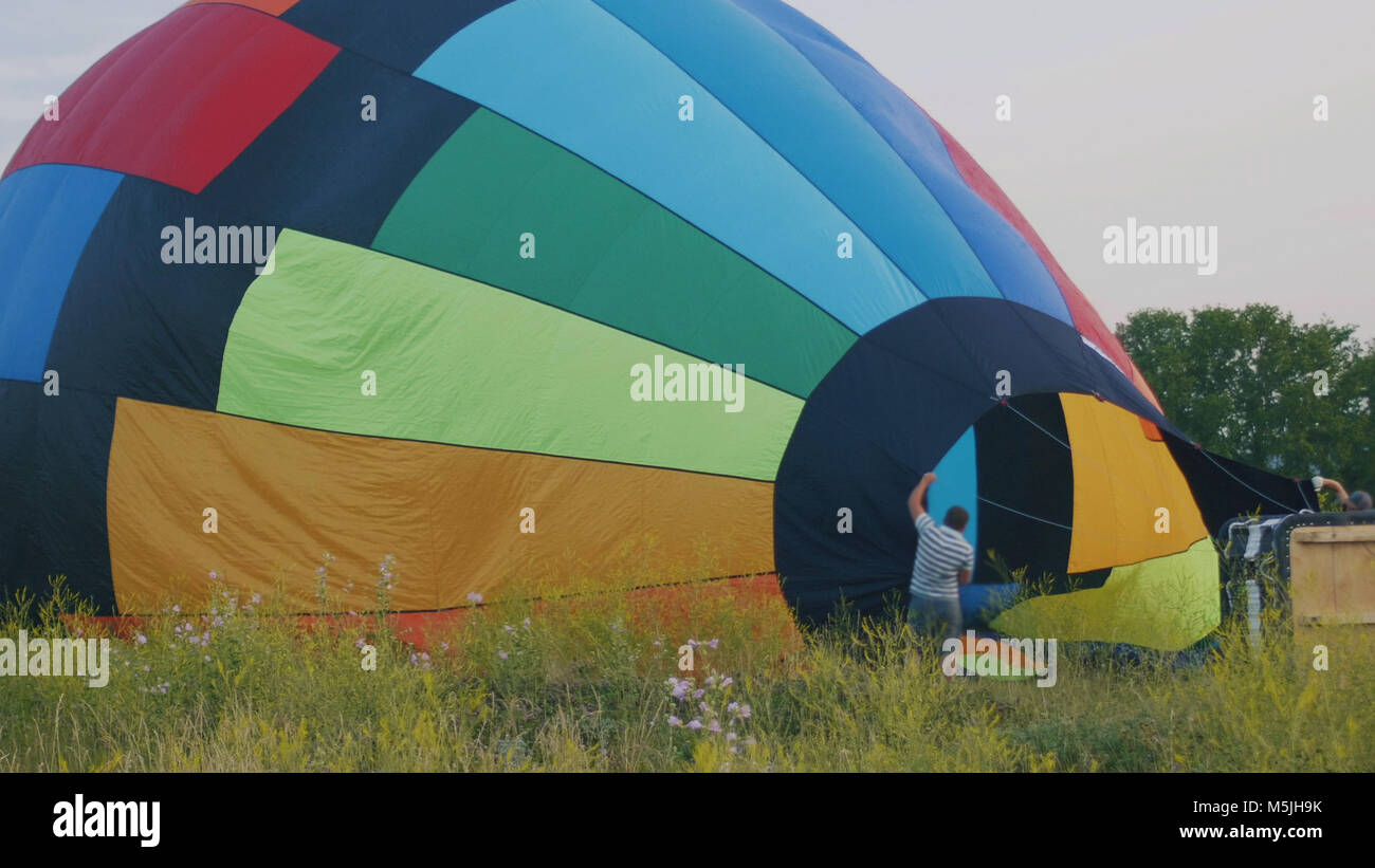 Crew inflate a big colorful hot air balloon at summer field Stock Photo