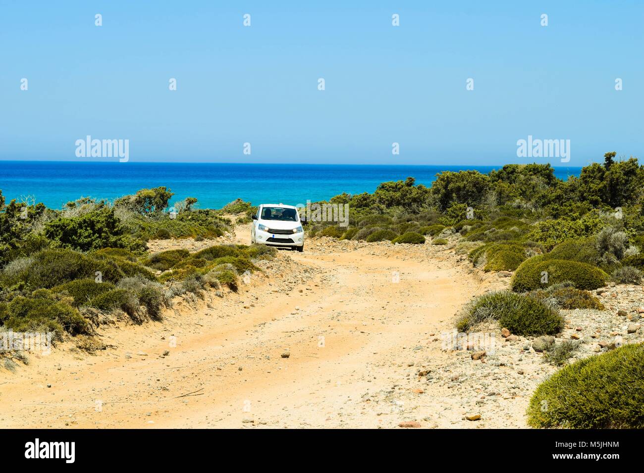 Car driving on a stony path in front of the ocean on Kos island Stock
