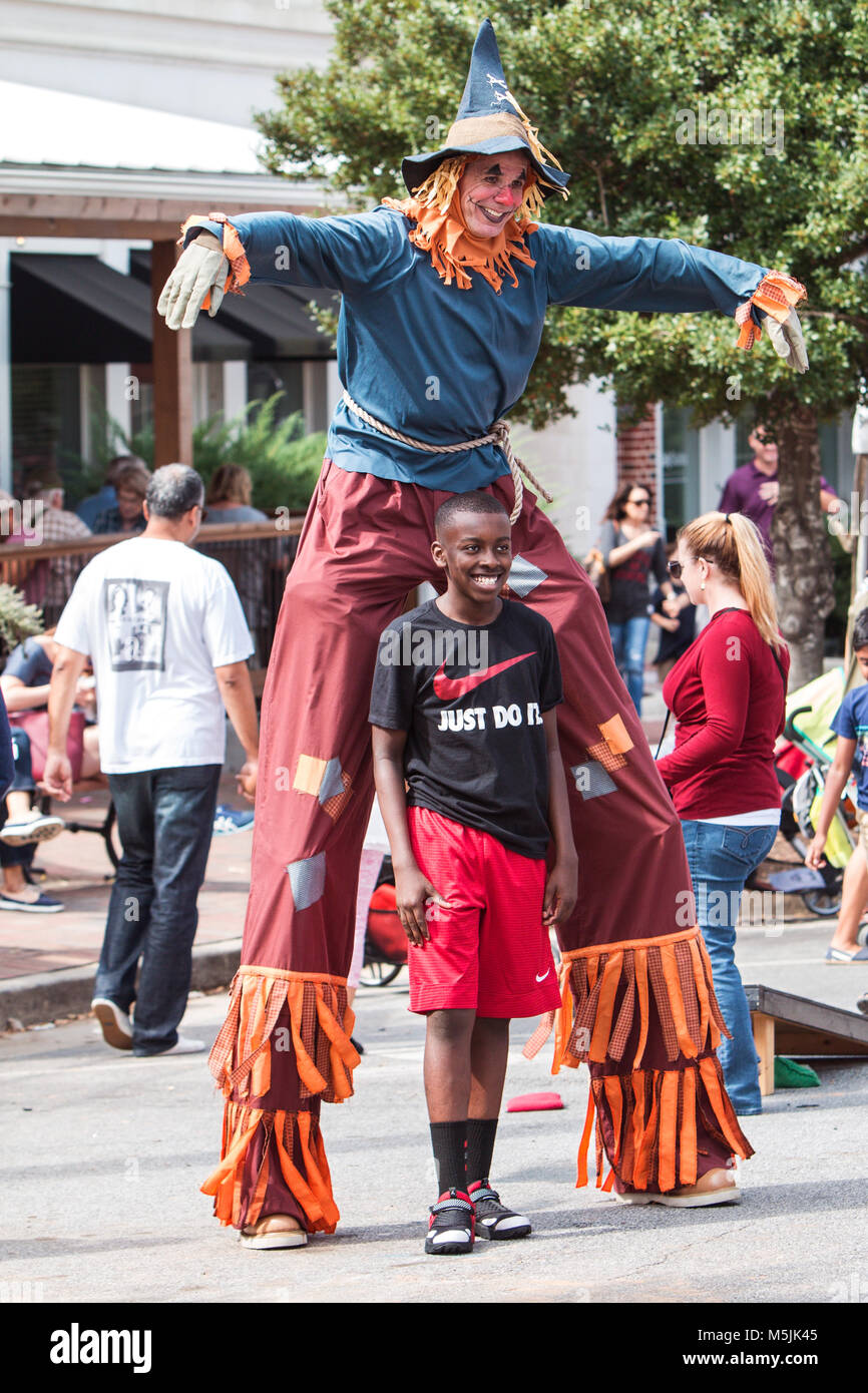 A man dressed in a scarecrow costume on stilts poses for a picture with
