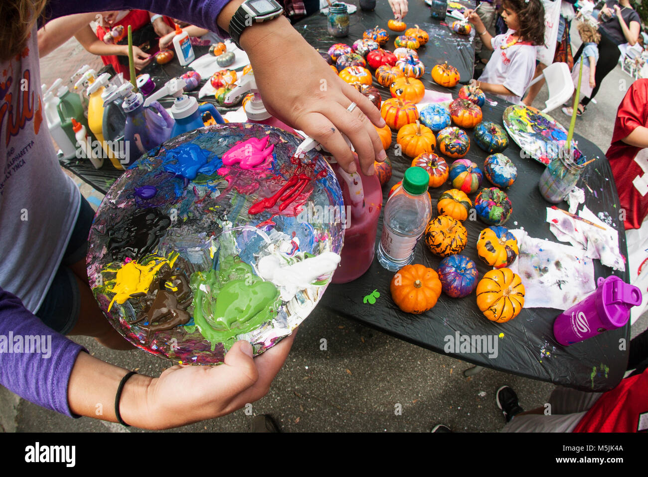 A woman squirts oil paint onto a palette to paint miniature pumpkins at the Scarecrow Harvest fall festival in Alpharetta, GA, on September 30, 2017. Stock Photo