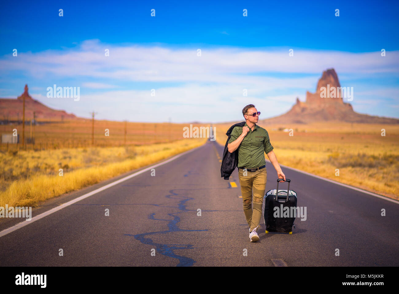 Young traveler with a suitcase walking on a road in Arizona Stock Photo