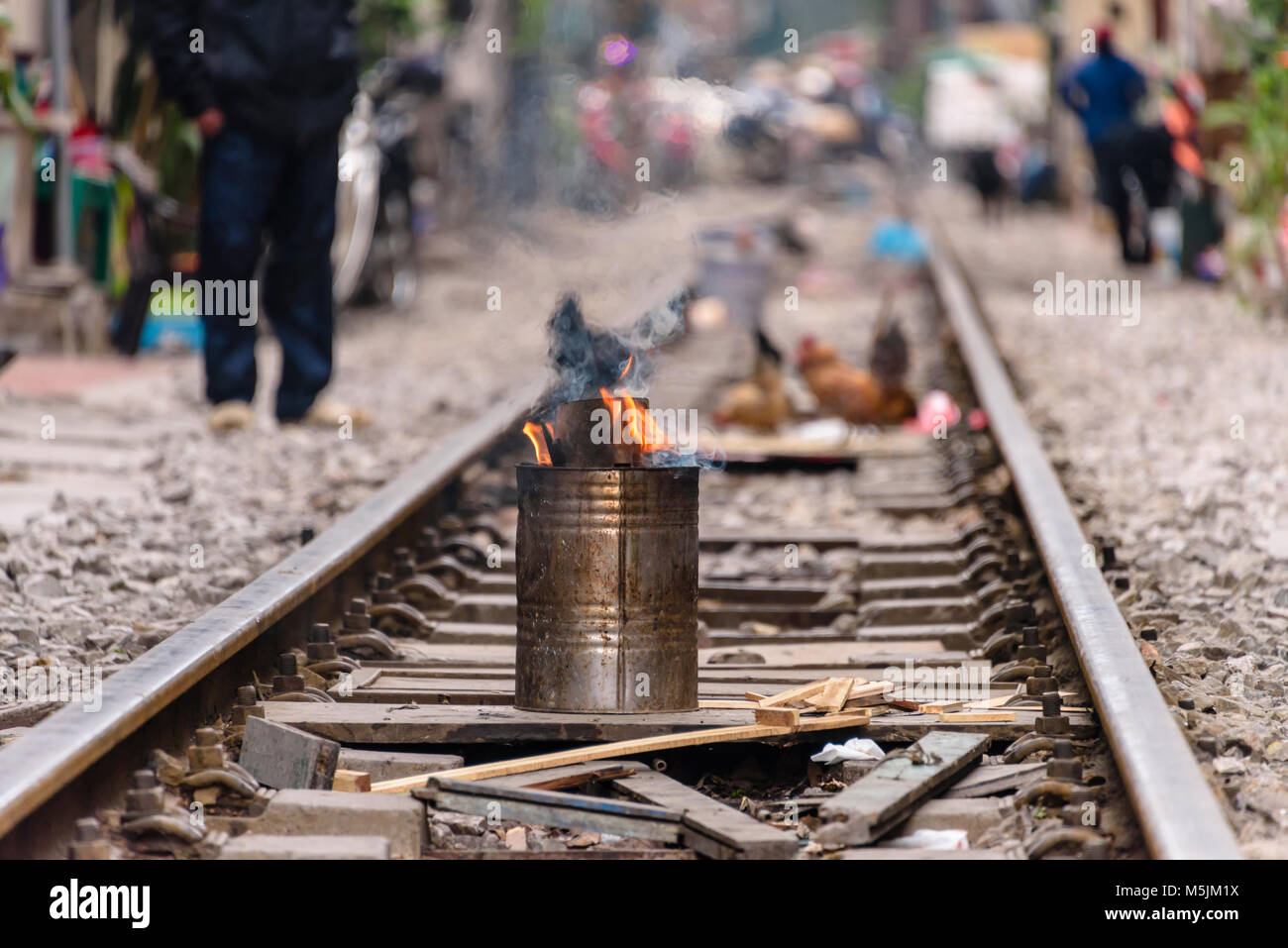 A meal is cooked in a metal stove in the middle of railway tracks with chickens in the background at 'Railway Street' in Hanoi, Vietnam. Stock Photo