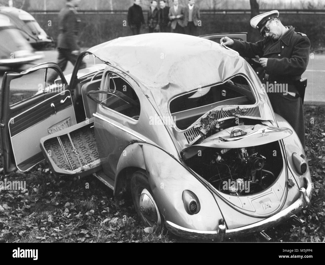 Police officer inspects VW beetle with total damage,1960s,Berlin,Germany Stock Photo