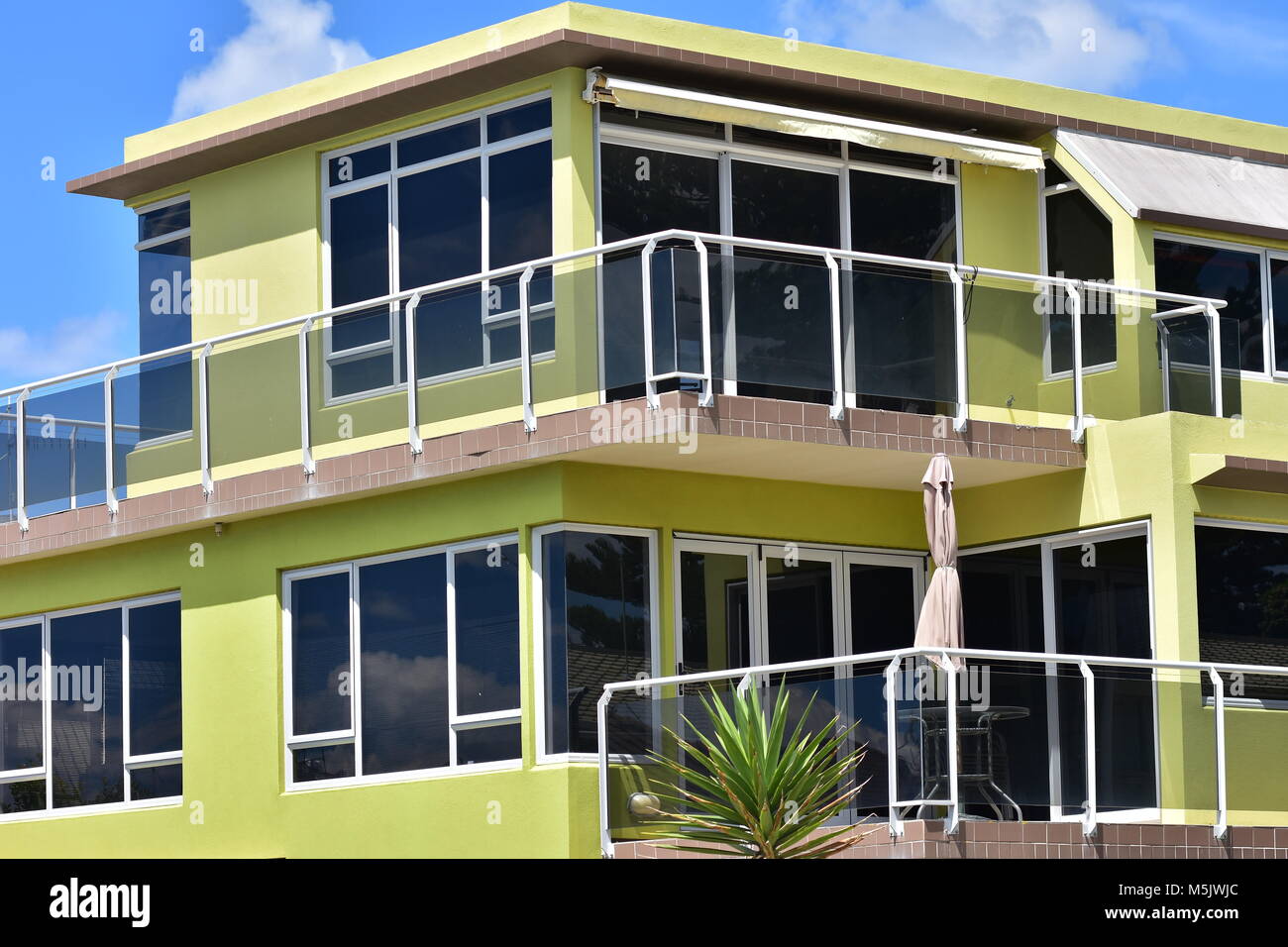 Yellow multi-story holiday house with verandas protected by glass railing and tinted glass windows. Stock Photo