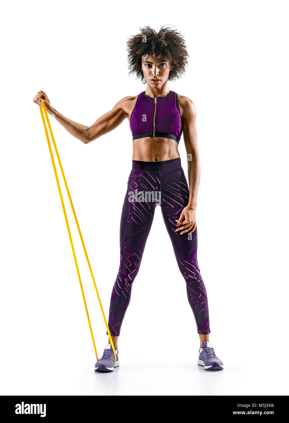 Strong girl using a resistance band in her exercise routine. Young african girl performs fitness exercises on white background. Strength and motivatio Stock Photo