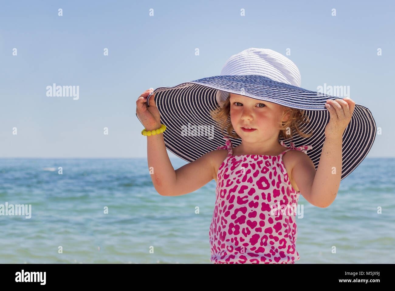 Funny little girl in a big striped hat on the beach Stock Photo - Alamy