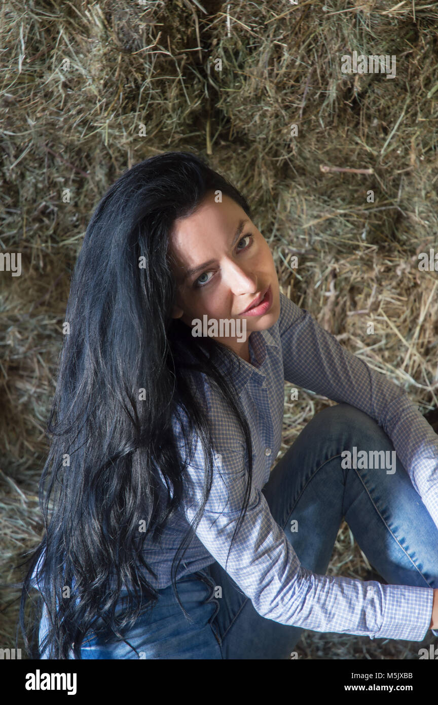 Long black haired female looking at camera while sitting in barn Stock Photo