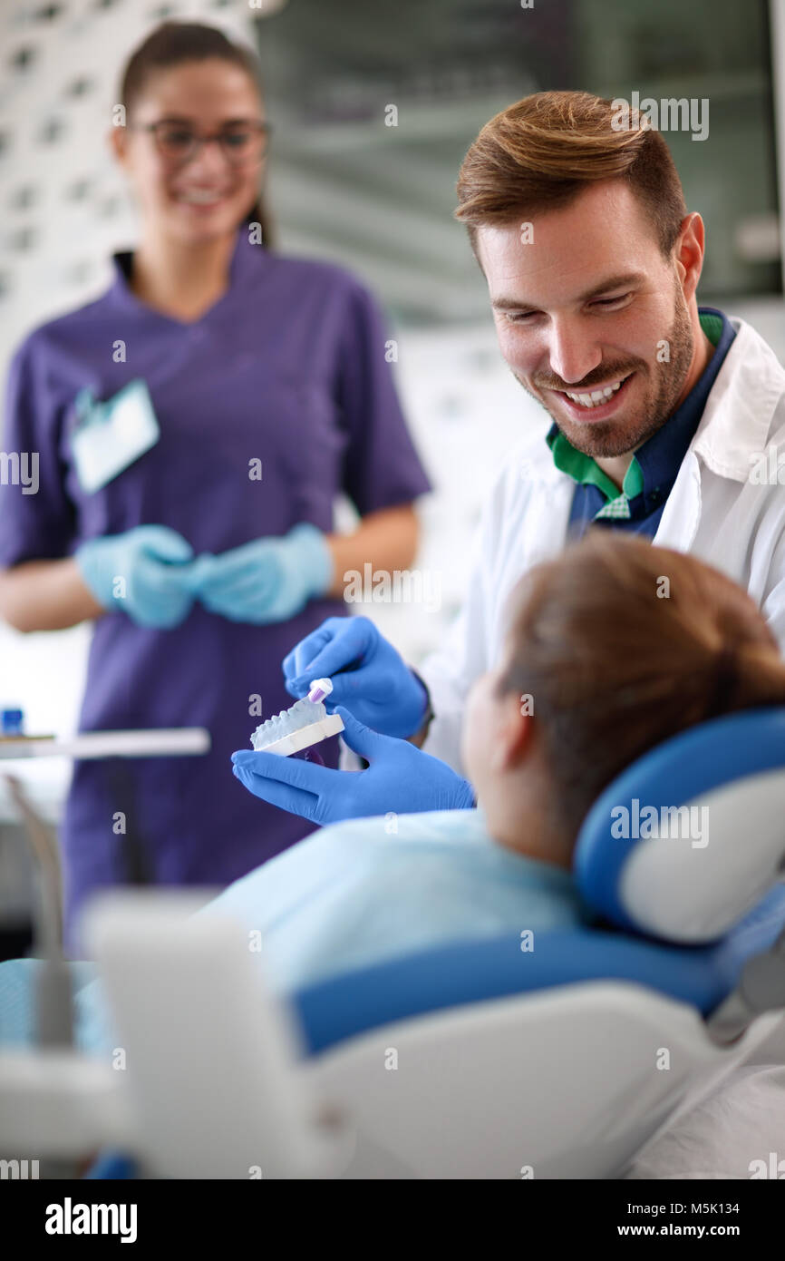 Dentist shows to young patient properly brushing teeth on model of