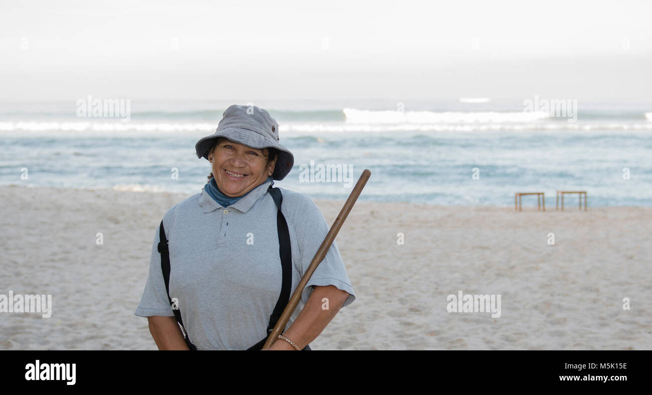 Older Smiling & Friendly Mexican Woman Working on a Resort Beach Raking ...
