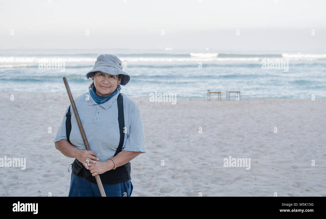 Older Smiling & Friendly Mexican Woman Working on a Resort Beach Raking ...