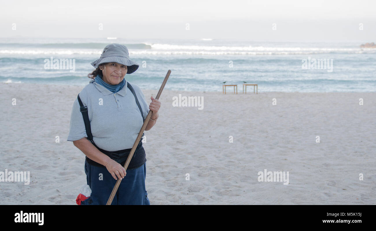 Older Smiling & Friendly Mexican Woman Working on a Resort Beach Raking ...