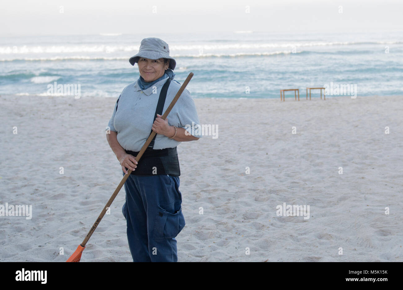 Older Smiling & Friendly Mexican Woman Working on a Resort Beach Raking ...