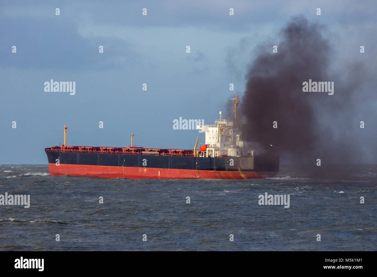 Industrial cargo ship causing air pollution leaving the Port of Rotterdam. Stock Photo