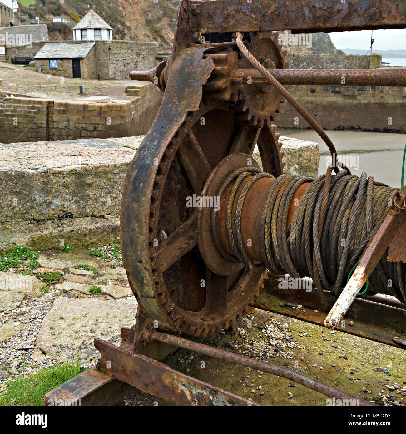 Old boat winch with rusty gear wheels and cogs, and steel cable, Charlestown Harbour slipway, Cornwall, England, UK Stock Photo